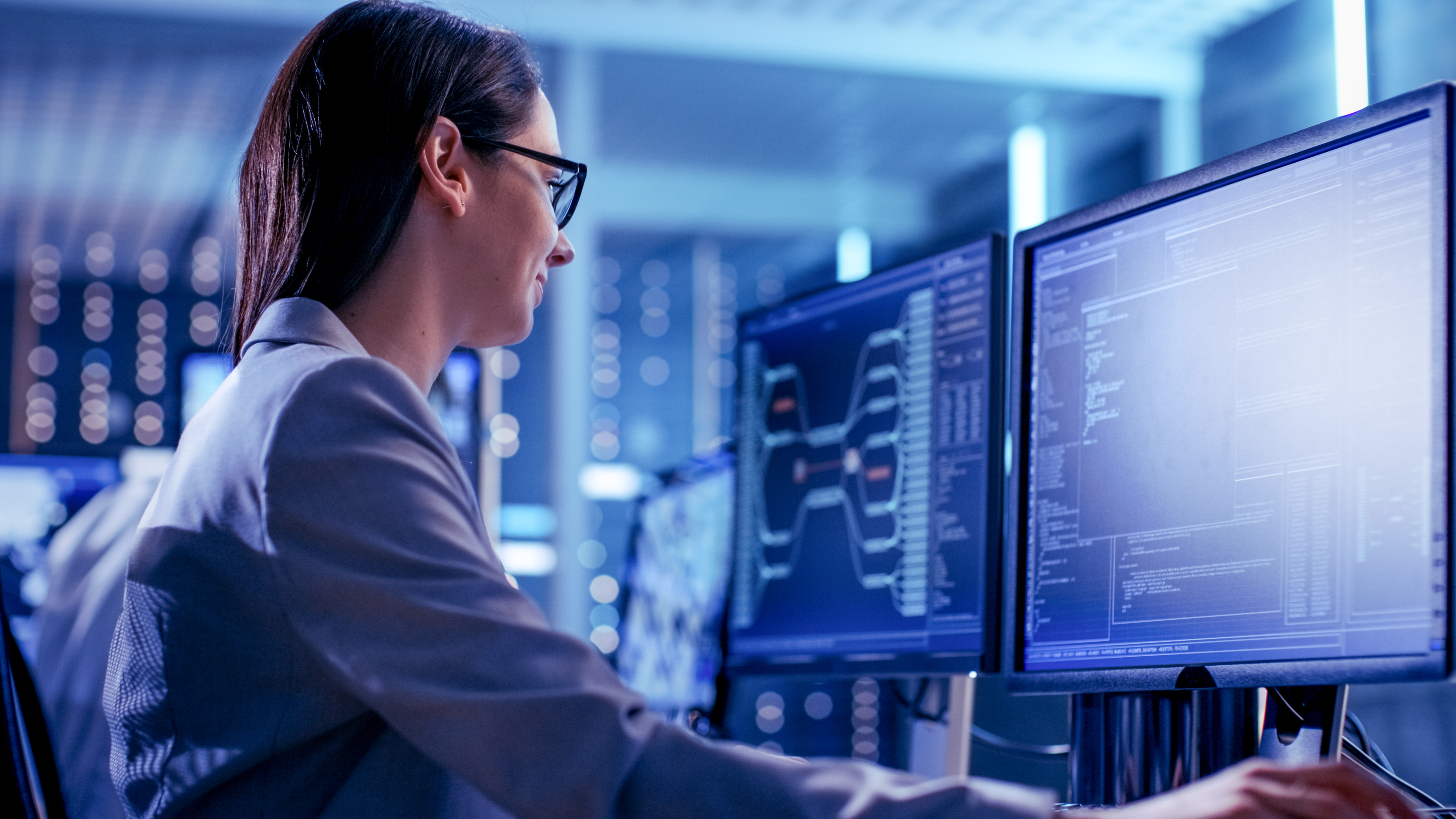 Close-up Shot of Female IT Engineer Working in Monitoring Room. She Works with Multiple Displays.